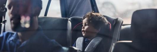 Parent driving with a toddler safely placed in the car's backseat.
