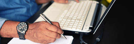 Close-up of a man’s hands, ready to take notes while following training on his laptop
