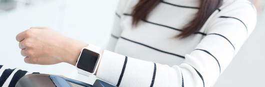 A woman holds her smartwatch up to a grey scanner