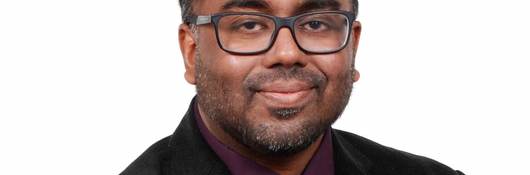 Anura Fernando wears a black jacket, burgundy shirt and grey tie for his corporate picture.