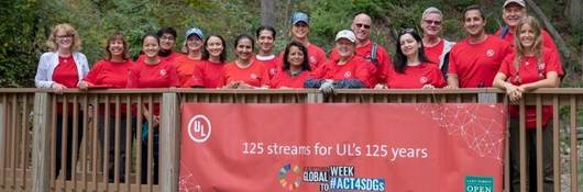 UL employees proudly pose on a wooden bridge on which has been hung a banner announcing 125 streams for 125 years.