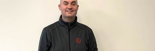 Seán Flannagan poses for EWeek picture. He's wearing a dark grey jacket with the red UL logo on its left pocket.