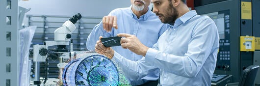 Two Engineers Works with Mobile Phone Using Augmented Reality Holographic Projection 3D Model of the Engine Turbine Prototype