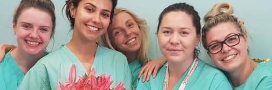 Five nurses wearing green scrubs, one who is holding a bouquet of flowers, pose for a picture. 