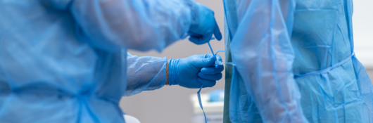 Medical worker ties a blue medical gown onto another worker.