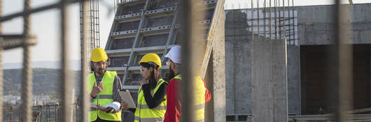 Three construction workers on roof of building with construction material, including concrete block and metal beams all around them