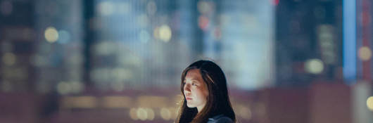 Woman outside on rooftop alone with cityscape in the background.