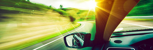 View out of a car on a road with sunlight by left side of the windshield