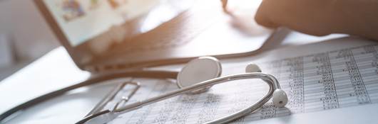Laptop on table beside stethoscope and medical chart