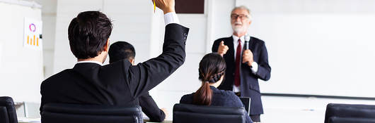 Business man raising hand in a classroom setting