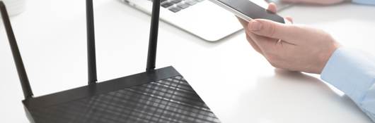 Wireless router positioned next to a laptop and mobile phone on a white table.