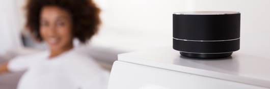 Close up of smart speaker with woman in blurred background