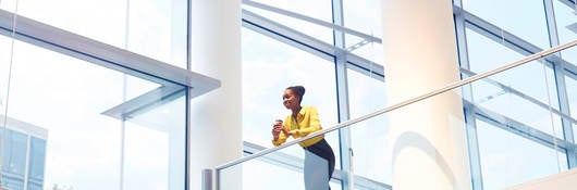 A Black woman looks down from the second floor of an interior office building.