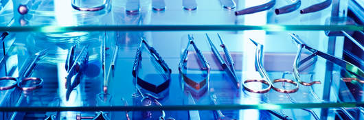 Medical tools sit on a shelf under the blue glow of ultraviolet light, used as a germicidal disinfectant.