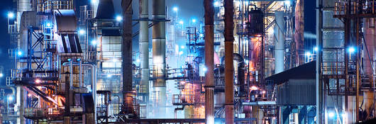 A brightly lit commercial oil refinery is shown at night.