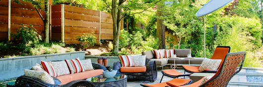 Outdoor furniture including sofa, chairs, table and umbrella in a sunny patio setting