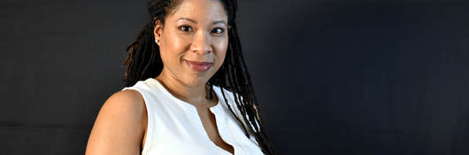 LaTanya Schwalb poses confidently wearing a white sweater while standing in front of a dark background.