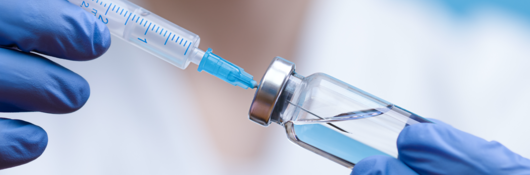 Gloved hand holding a vaccine vial and syringe