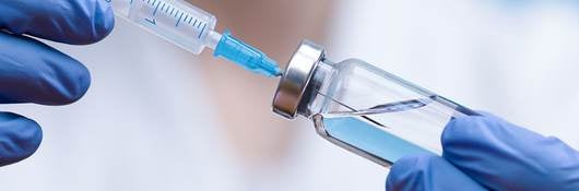 Healthcare worker wearing blue latex gloves hold syringe and vial of drug