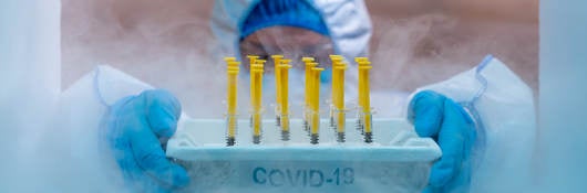 Medical worker with gloved hands inside a cold chamber holding a tray of COVID vaccines 