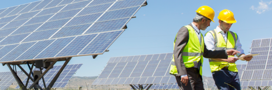 Workers reviewing an engineering report, with solar panels behind them
