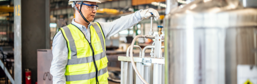 Man with yellow vest adjusting knob on gas tank in factory