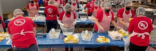 Wide shot of UL employees in red shirts packing meals for Impact 100. 