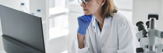 Woman in rubber gloves sitting at computer in lab