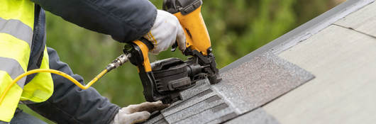 Roofer using nail gun to attach shingles to a roof