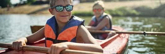 Children in life jackets rowing a canoe.