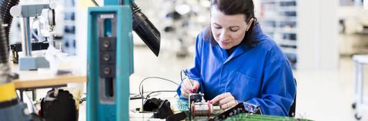 Mid adult female electrician working on circuit board at desk in industry.