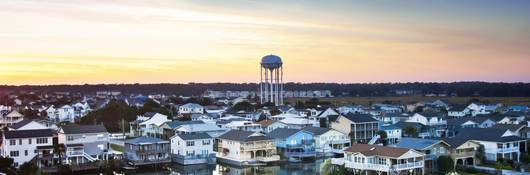 Houses sit along a saltwater inlet with a water tower in the background.