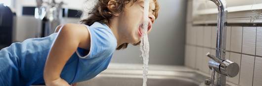Small boy drinking water out of faucet.