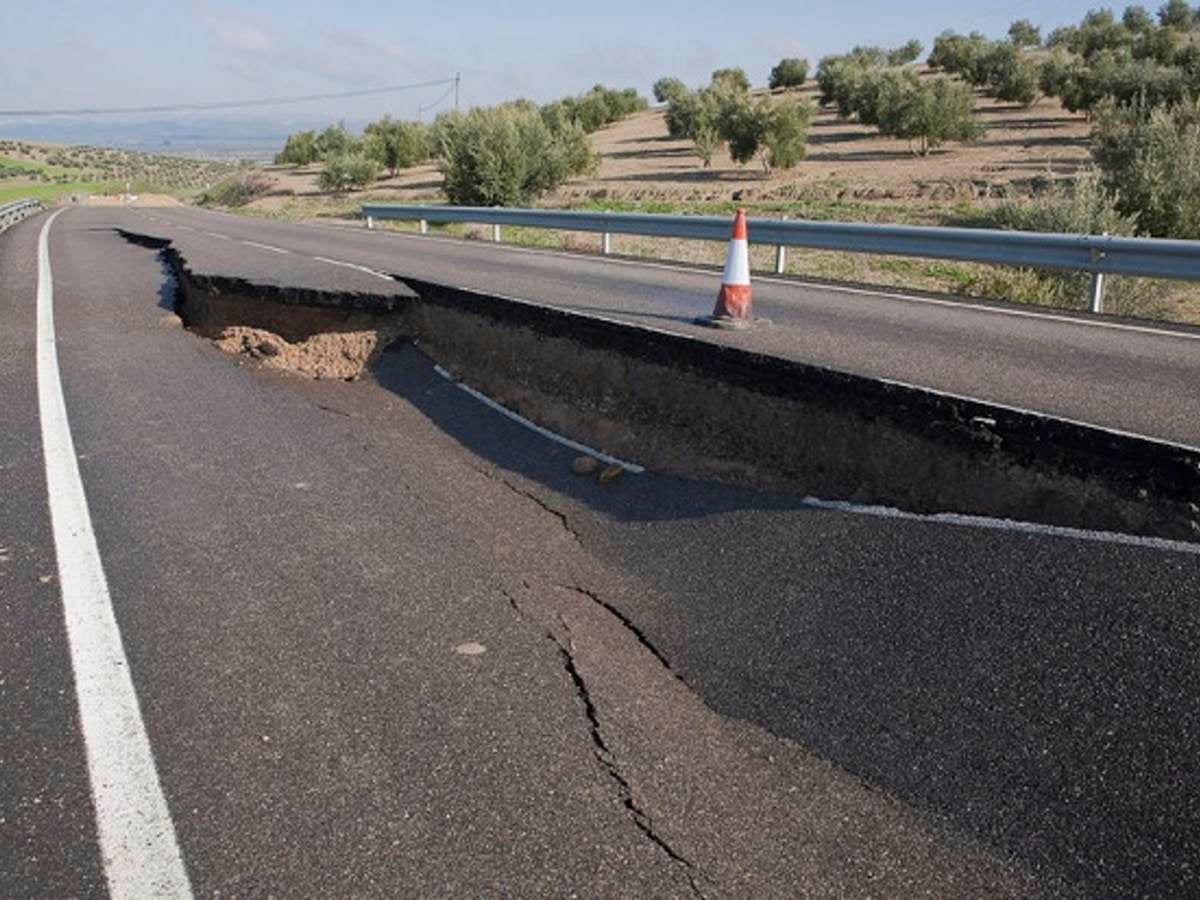 A two-lane road with a giant hole, caused by a landslide, in the middle of the road.