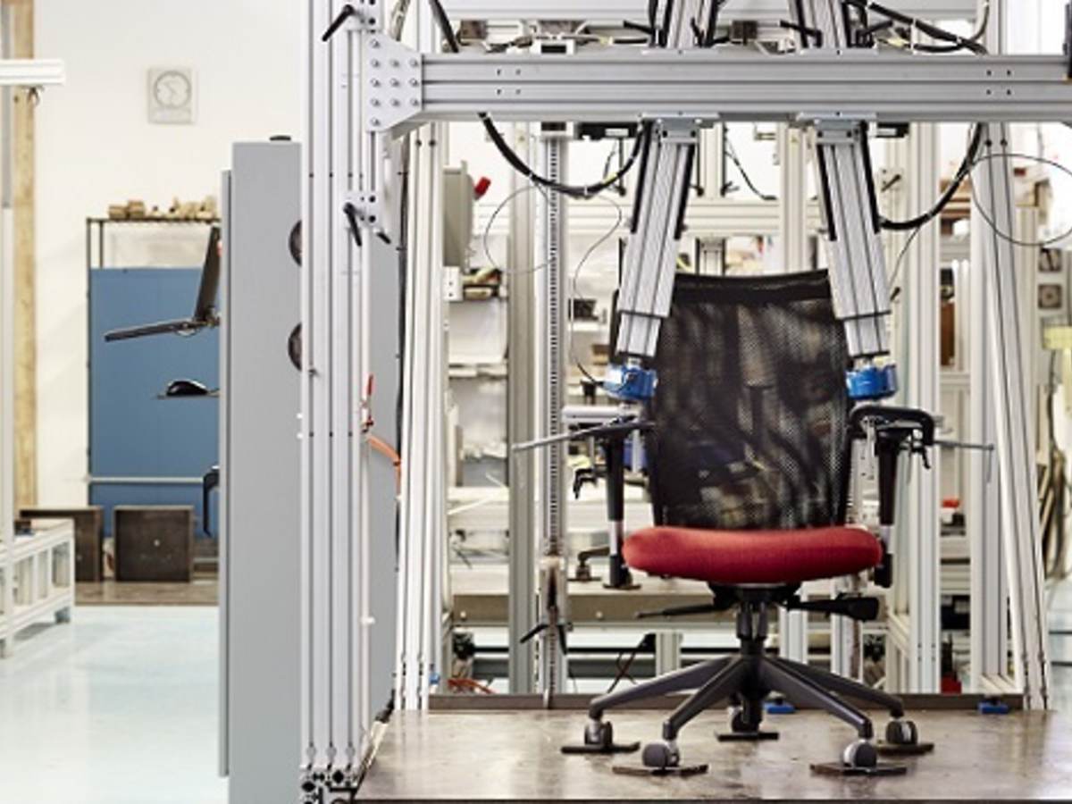 Black office chair with red seat cushion undergoes durability test at Holland, Michigan lab