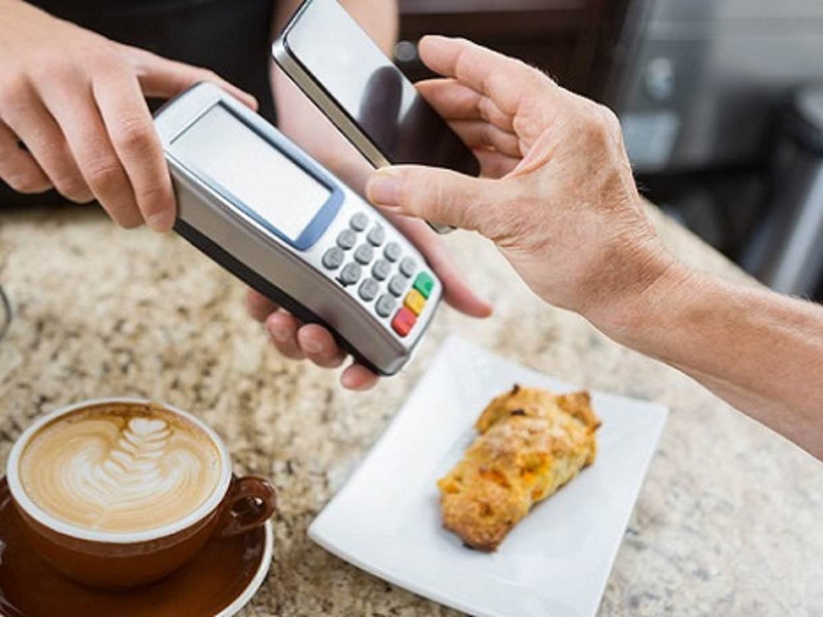cropped image of customer paying through mobile phone over electronic reader at cafe counter