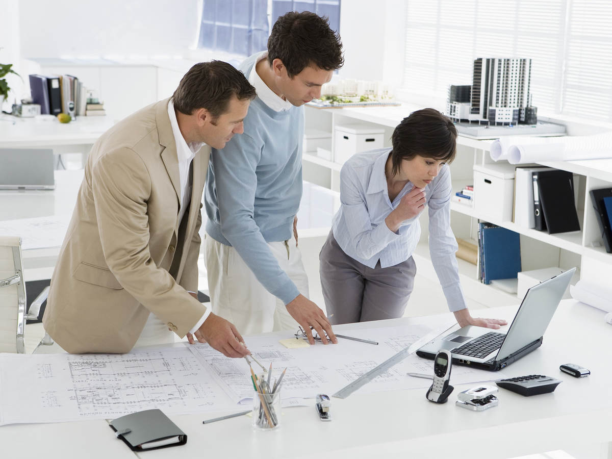 Three people in an office confer over computer and floor plans.