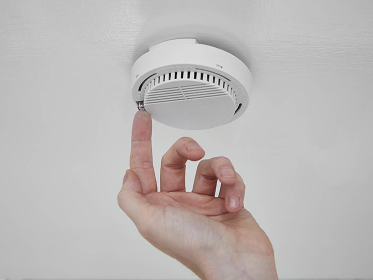 A person pressing a button on a fire alarm. 
