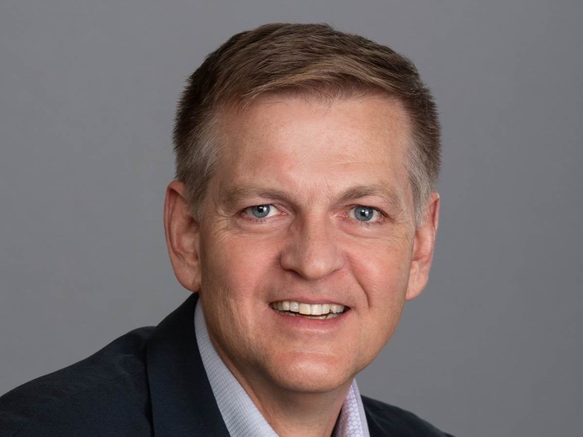 Craig Rowlands poses against a grey background. He is wearing a black jacket with a grey shirt. 