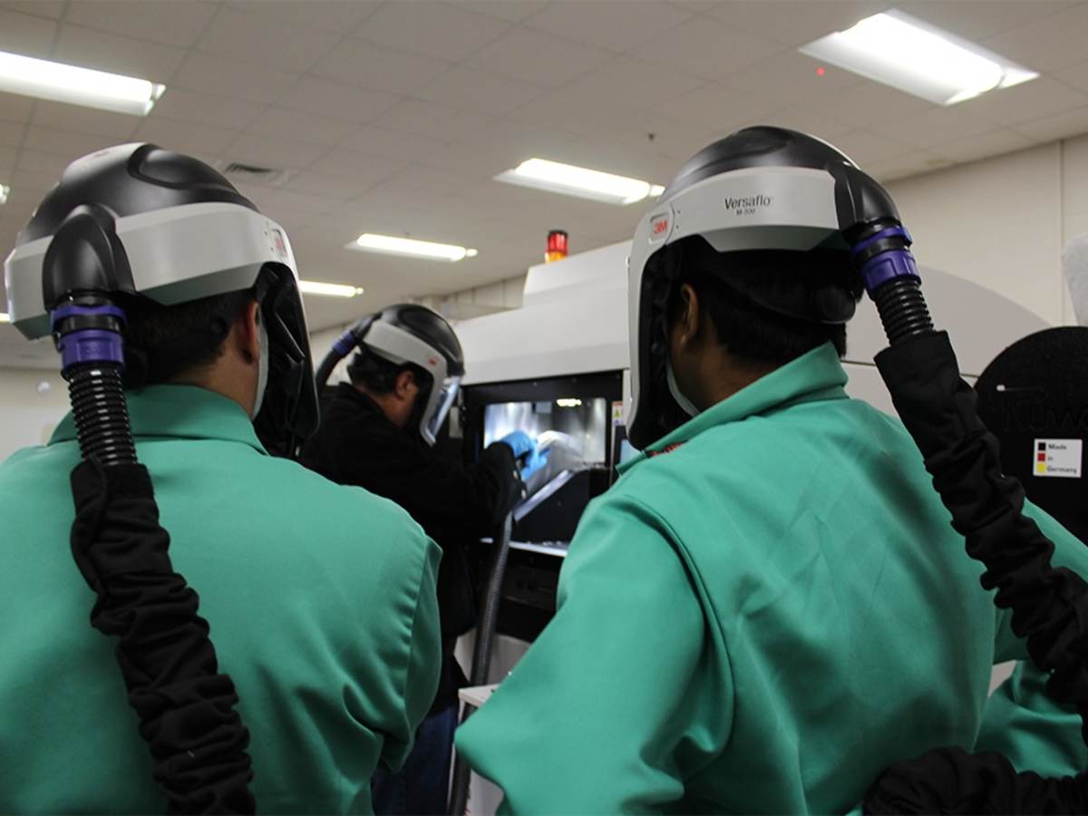 Two observers watch a worker using an industrial 3D printer.