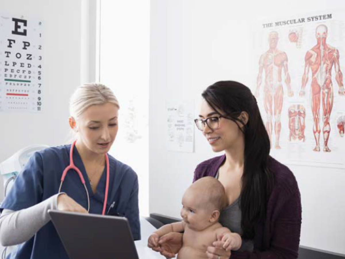 Mom with baby on lap in examining room talking to woman