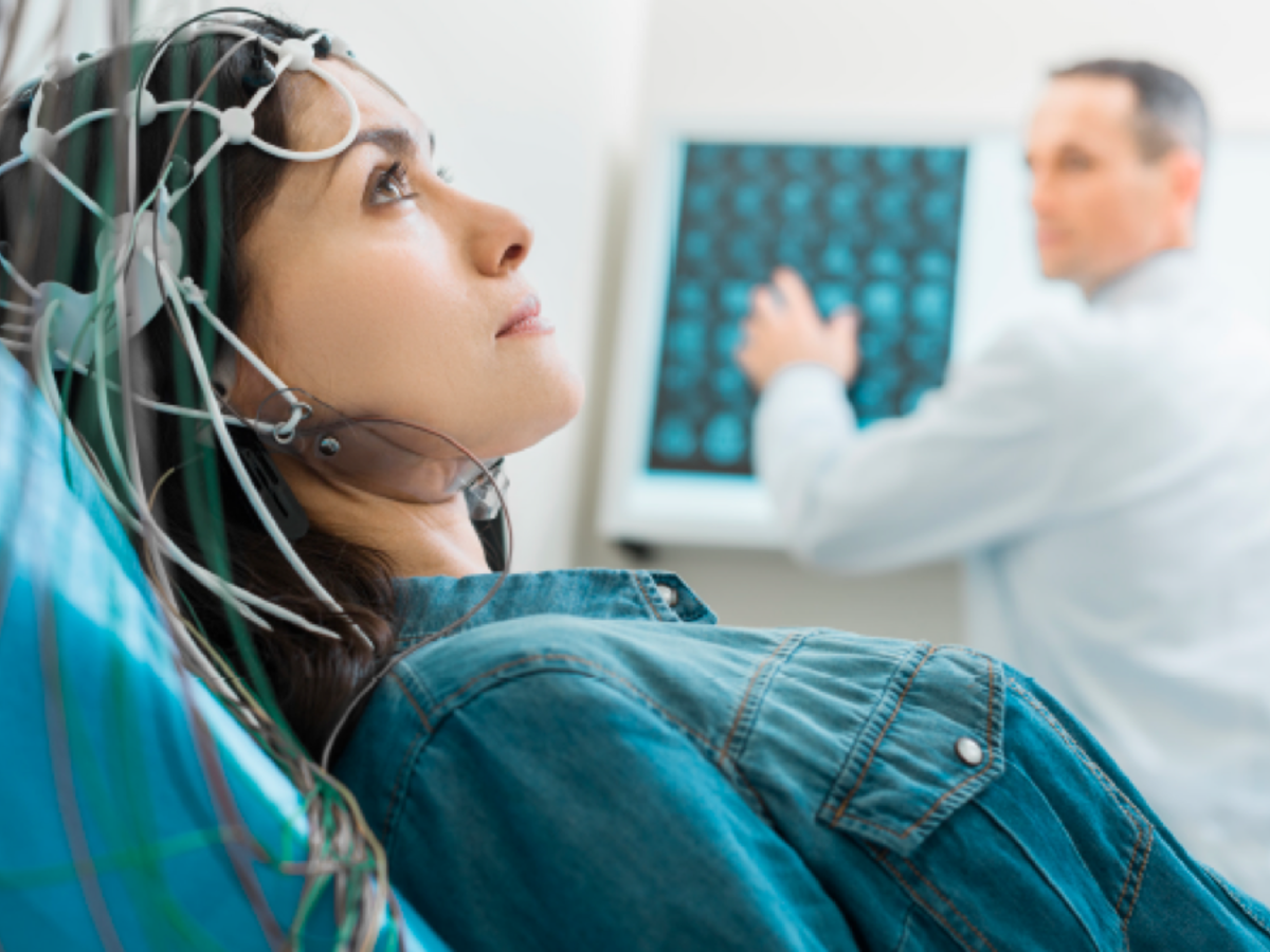 Woman in doctors office with sensors on her head - man in background by screen
