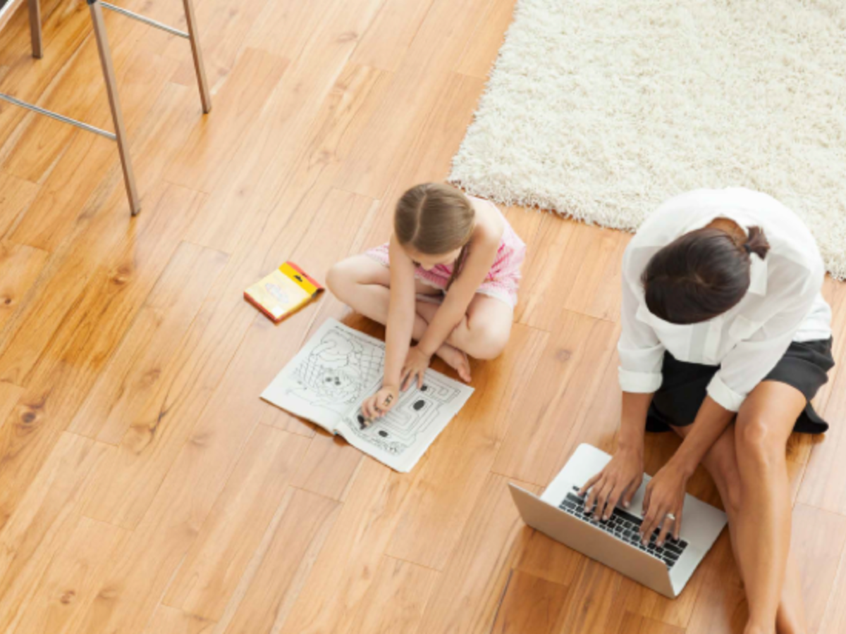 Overhead shot of woman on computer & young girls with coloring book sitting on wood floor