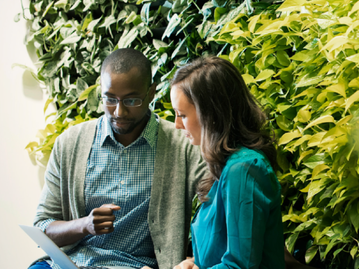 man and woman sitting next to one another in front of foliage