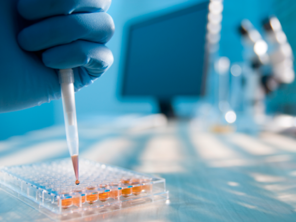 Gloved hand in lab with dropper and computer screen in background