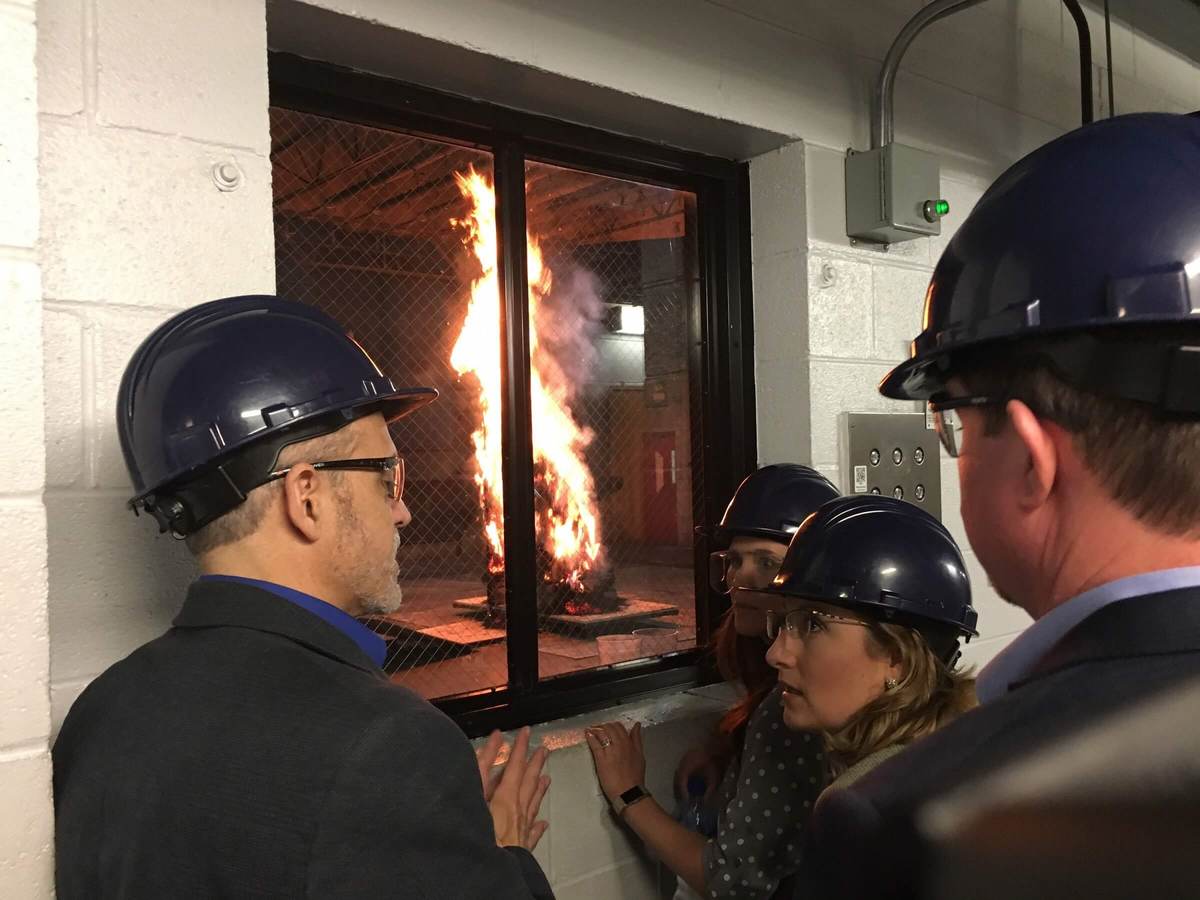 Four members of the JCI Fire Suppression team observe their antifreeze product in action at UL laboratories. An undetermined object is on fire and the team is looking through a window at the event.