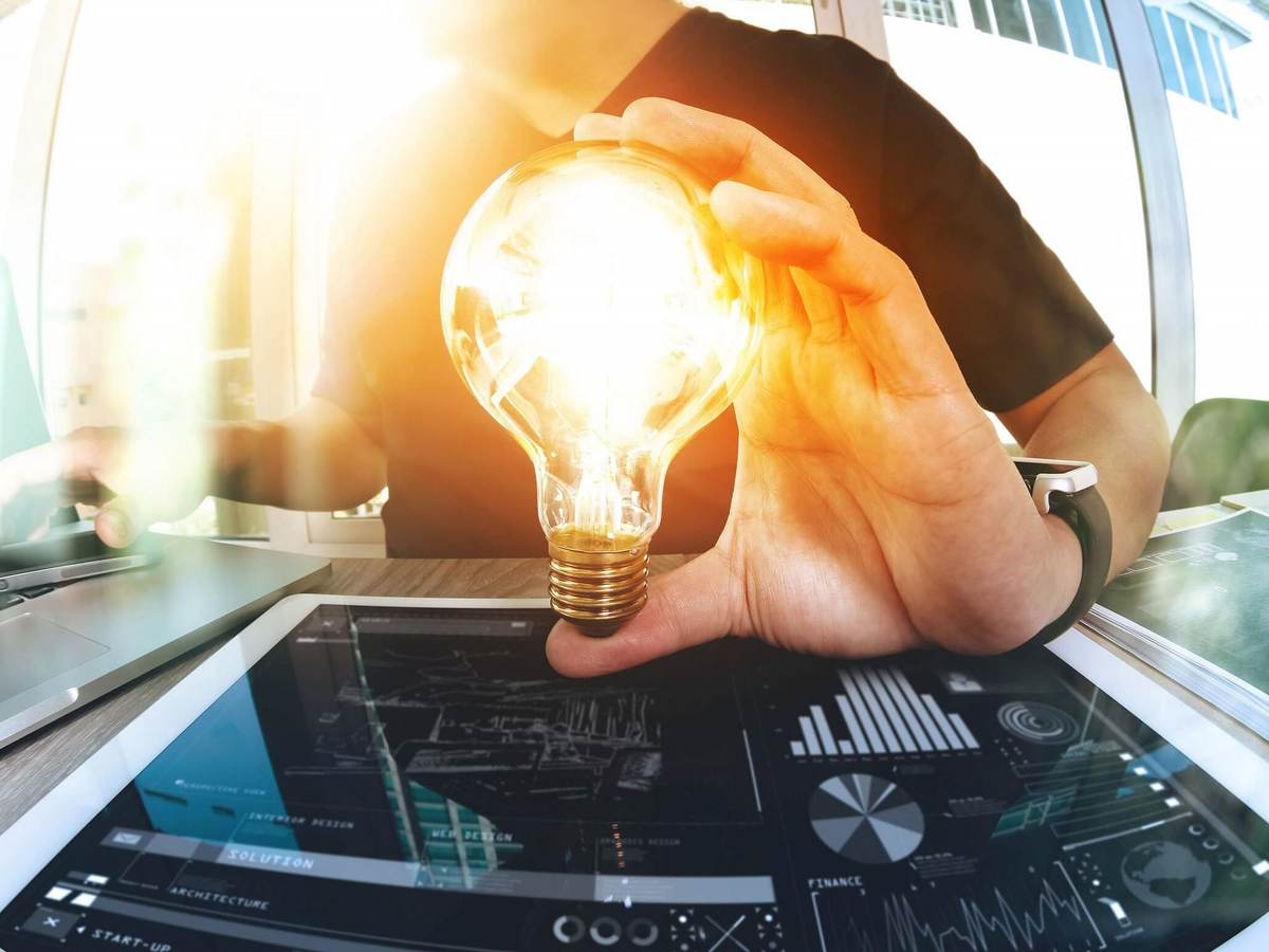 A man in a burgundy shirt holds a light bulb in his left hand, which is placed over a smart pad.