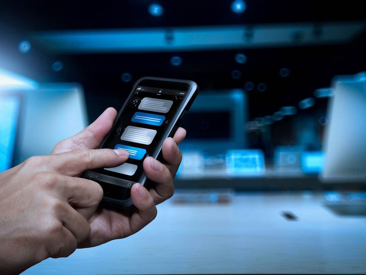A hand holds a smartphone while the other hand converses with a chatbot.