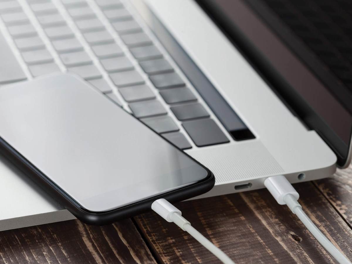 The white cable of a mobile phone draws power from a laptop.