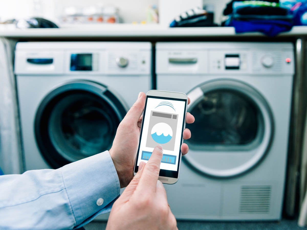 A man using his phone thats connected to a washing machine